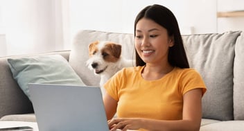 woman typing on laptop sitting with a jack russell terrier